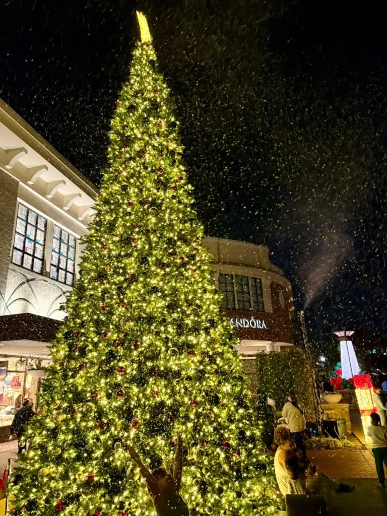 Snow machine snowfall over a giant lit Christmas tree at a shopping center
