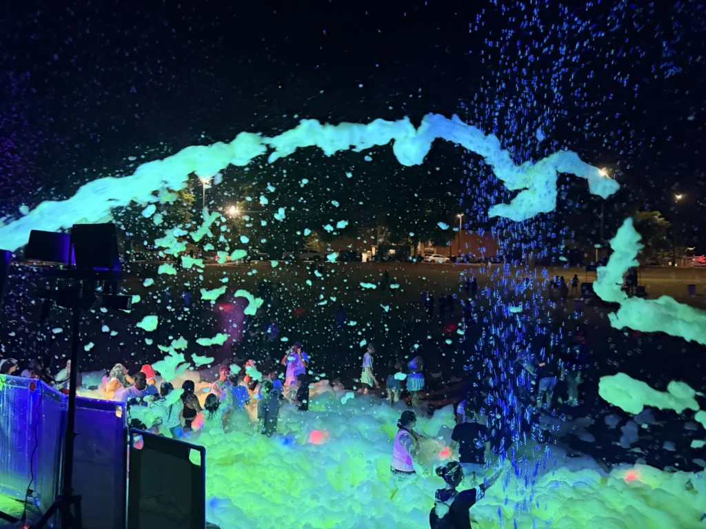 Wide view of a large crowd in glowing foam under blacklights in Athens, Alabama